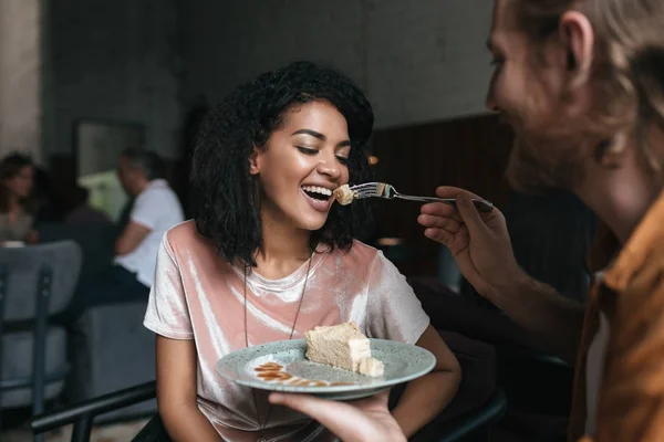 Retrato de una joven afroamericana comiendo pastel en un restaurante. Joven alimentando a su novia en la cafetería — Foto de Stock