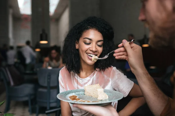 Retrato de una joven afroamericana comiendo pastel en un restaurante. Joven alimentando a su novia en la cafetería — Foto de Stock