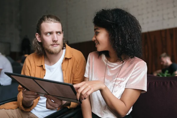 Menina afro-americana bonita com cabelo encaracolado escuro e menino com cabelo loiro pensativo olhando um para o outro no café — Fotografia de Stock