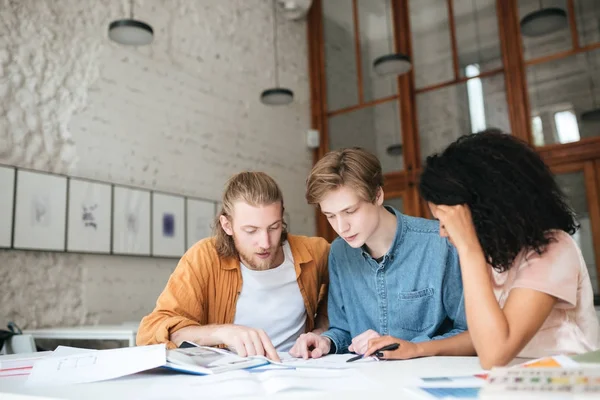 Ritratto di giovani che lavorano in ufficio. Due ragazzi con i capelli biondi e una ragazza con i capelli ricci scuri seduti e che studiano insieme in classe — Foto Stock