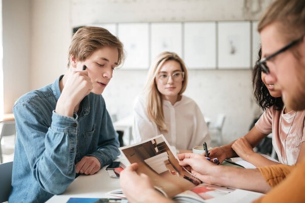 Portrait of young people thoughtfully looking at photo in journal. Group of cool guys working on new project in office — Stock Photo, Image