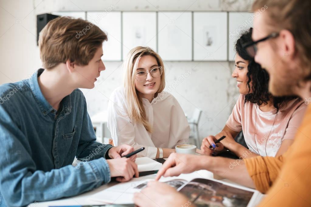 Portrait of young people sitting in office and happily looking at each other while discussion something