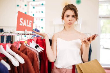 Satış giyim işkencesi duran ve amazedly kamera seyir butik beyaz top genç kız