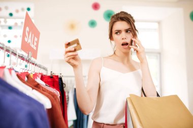 Satış giyim işkencesi duran ve amazedly kredi kartını butik içinde seyir beyaz top düşünceli kız