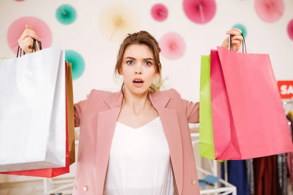 Портрет молодой девушки, удивительно смотрящей в камеру с красочными сумками в руках в магазине одежды — стоковое фото