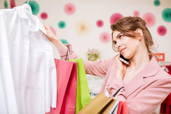 Portré, fiatal lány, pink dzseki beszél neki mozgatható telefon-val színes bevásárló táskák, kezében a közben kiválasztja ruhákat, butik — Stock Fotó