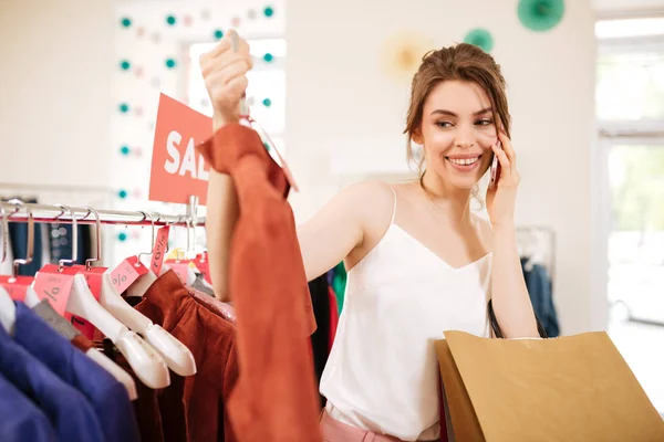 Szép lány fehér felső áll közel eladó ruhák rack a kezét, és boldogan nézett rajta butik póló — Stock Fotó
