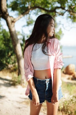 Pembe gömlek ve beyaz bluz ayakta ve sersem bir kenara arka plan üzerinde deniz manzaralı seyir siyah saçlı genç güzel kız portresi