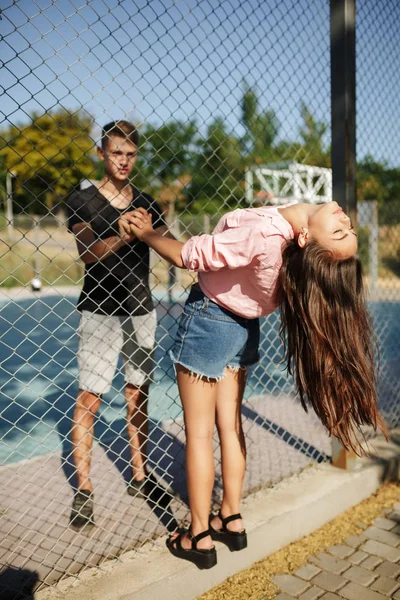 Unga vackra paret står mellan mesh staket och hålla händerna på varandra på basketplan — Stockfoto