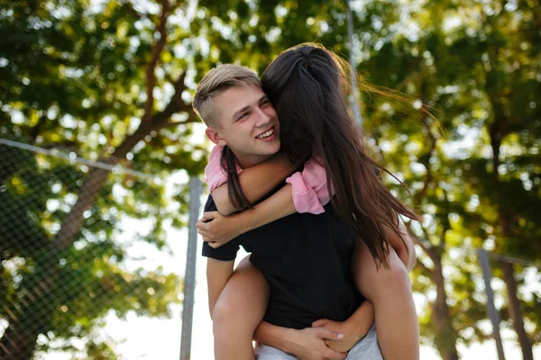 Porträt eines fröhlichen Jungen, der ein hübsches Mädchen auf dem Rücken hält und verträumt zur Seite schaut, während er Zeit im Park verbringt — Stockfoto