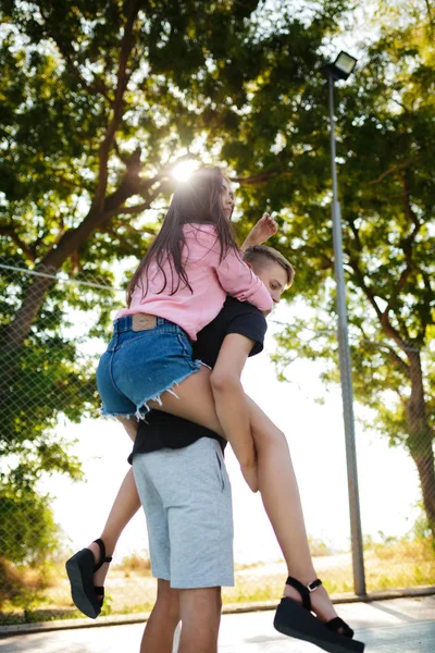 Porträtt av ung pojke håller vacker flicka på ryggen och ha roligt medan spendera tid i parken tillsammans — Stockfoto