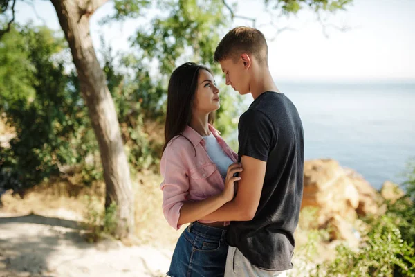 Porträt eines jungen schönen Paares stehend und verträumt auf einander blickend, während sie Zeit miteinander verbringen, mit Meerblick im Hintergrund — Stockfoto