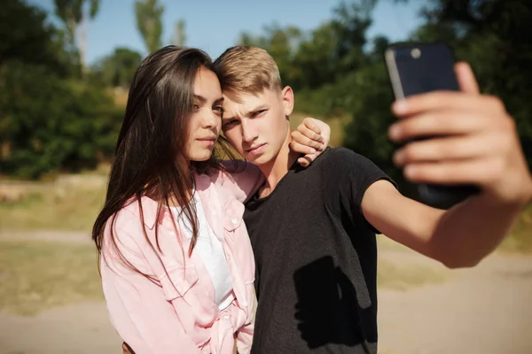 Porträtt av ung trevlig par stå och göra selfie i park. Söta par att ta foton på frontal mobilkamera — Stockfoto