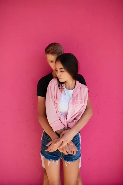 Retrato de jovem belo casal de pé e abraçando uns aos outros na parte traseira rosa isolado — Fotografia de Stock