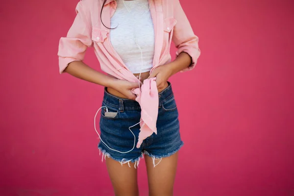 Foto de cerca del cuerpo delgado de la muchacha de pie en pantalones cortos de mezclilla y camisa sobre fondo rosa aislado — Foto de Stock