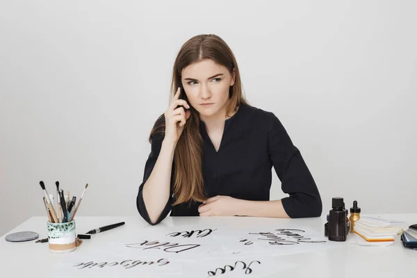 Портрет женщины, сидящей за белым столом и разговаривающей по мобильному телефону, всерьез глядя в сторону — стоковое фото