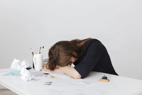 Foto de la señora cansada sentada en el escritorio blanco y durmiendo mientras se apoya la cabeza en sus manos aisladas —  Fotos de Stock