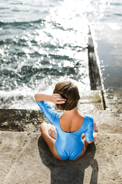 Schöne Frau, die mit dem Rücken sitzt und am Meer meditiert. Porträt einer hübschen Dame im Badeanzug, die Yoga praktiziert, mit atemberaubendem Meerblick im Hintergrund — Stockfoto
