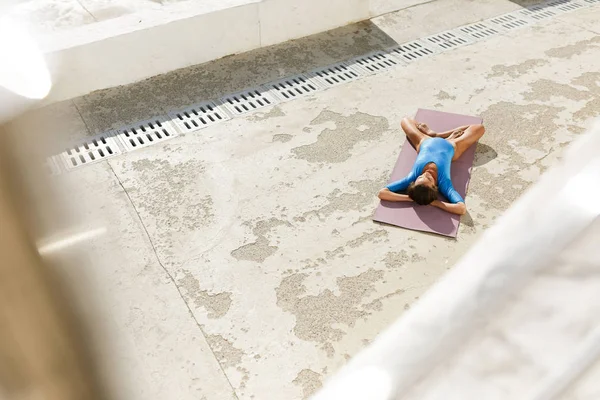 Foto einer jungen Frau mit dunklen Haaren, die auf einer Yogamatte liegt und Yoga macht. schöne Dame im blauen Badeanzug meditiert und praktiziert isoliert Yoga — Stockfoto