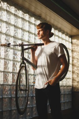 Ayakta ve bisiklet böyle bir eğilimi omzunda sersem bir kenara bakarken tutmak düşünceli çocuk. Klasik bisiklet ile ayakta ve cebine elini tutarak beyaz t-shirt genç adam