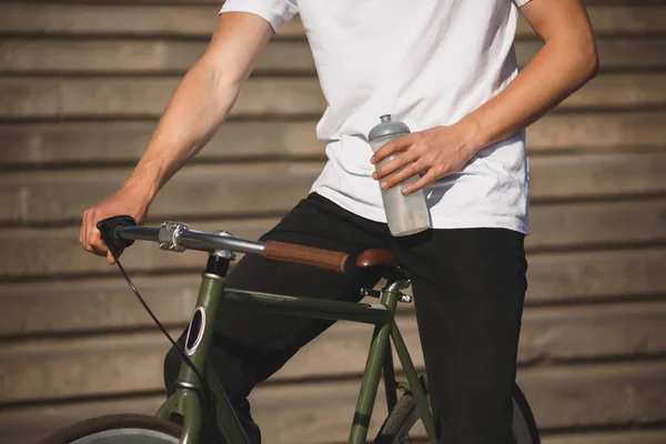 Zavřete fotografie těla člověka v bílém tričku s kolo a láhev vody v ruce. Fotografie z těla člověka jedoucího klasický kole — Stock fotografie