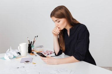 Beyaz masa başında oturan ve düşünceli izole telefonunu arayan genç güzel Bayan portresi