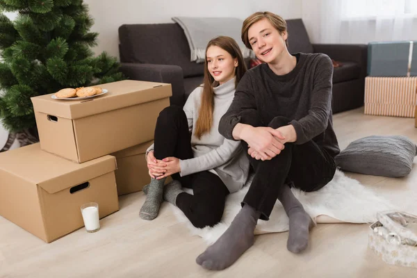 Portrait of beautiful girl and boy sitting on floor at home and happily looking in camera — Stok Foto