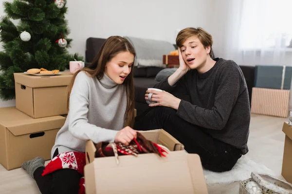 Güzel genç çift evde ve amazedly kutusunda arka plan üzerinde Noel ağacı ile seyir katta oturan portresi — Stok fotoğraf