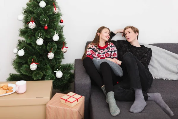 Evde kanepede oturan ve birbirinizle Noel ağacının yanında ile konuşmak güzel genç çift portresi — Stok fotoğraf
