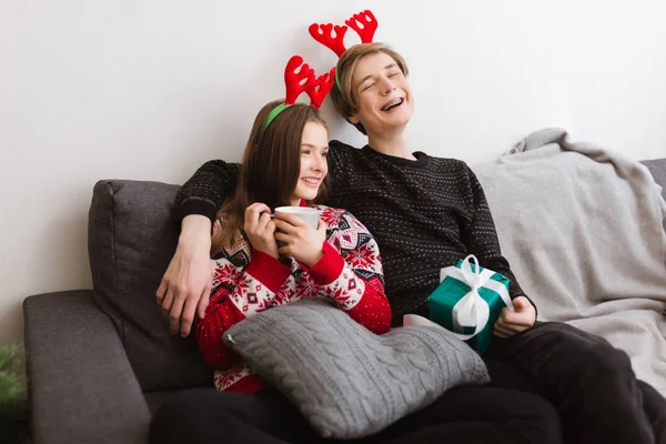 Retrato de jovem casal sorridente sentado no sofá em casa e usando chifres de veado enquanto alegremente passam tempo juntos — Fotografia de Stock