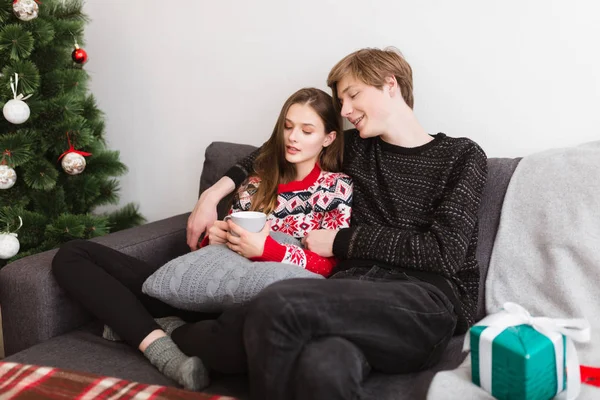 Evde kanepede oturan ve Noel ağacının yanında birlikte vakit genç güzel Çift — Stok fotoğraf