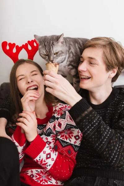 Porträt eines jungen coolen Paares, das zu Hause mit Eis in der Hand auf dem Sofa sitzt und glücklich Zeit miteinander verbringt, während es mit der Katze spielt — Stockfoto