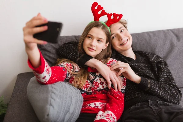 Retrato de una joven pareja sonriente sentada en un sofá en casa y tomando una autofoto divertida mientras pasan tiempo juntos — Foto de Stock