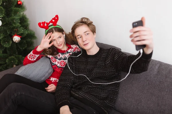 Kulaklıklar içinde evde kanepede oturan ve selfie birlikte vakit süre alarak genç güzel çift portresi — Stok fotoğraf