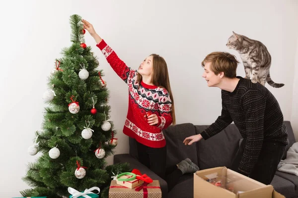 Evde kanepenin üzerinde duran ve çocuk ile kedi onun omuz ona yardım ederken Noel ağacı süsleme güzel kız portresi — Stok fotoğraf