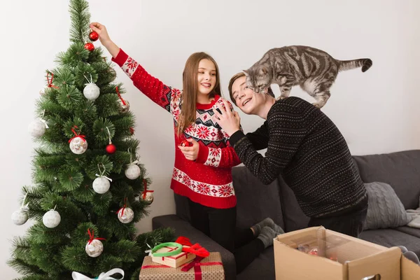 Evde duran ve birlikte Noel ağacı süsleme kedi ile genç güzel çift portresi — Stok fotoğraf