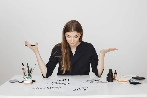 Retrato de jovem bonita senhora sentada na mesa branca com caneta na mão e olhando atenciosamente para papéis isolados — Fotografia de Stock