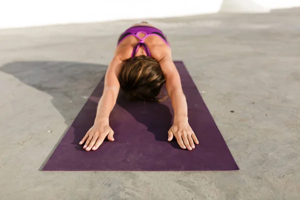 Portrait of woman sitting and pulling her hands while training yoga poses on purple yoga mat. Pretty lady with dark short hair in sporty top practicing yoga isolated