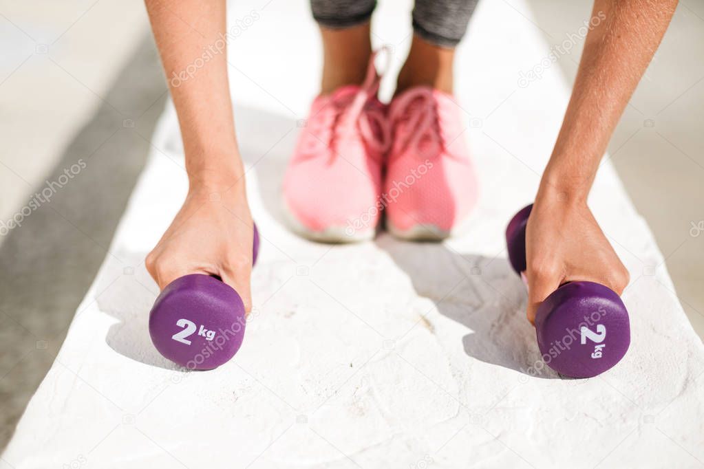 Close up photo of woman hands holding purple dumbbells and legs in pink sneakers isolated