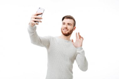 Selfie alarak ve ön kamera Merhaba beyaz arka plan üzerinde sallayarak neşeli yakışıklı adam