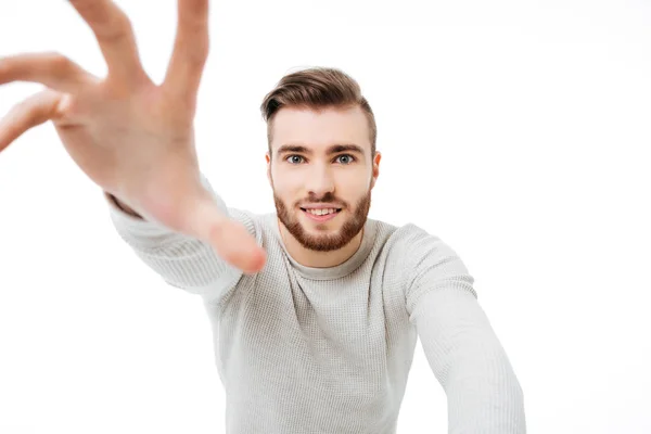 Handsome guy reaching out to the camera isolated. Young man trying to take your camera over white background — Stock Photo, Image