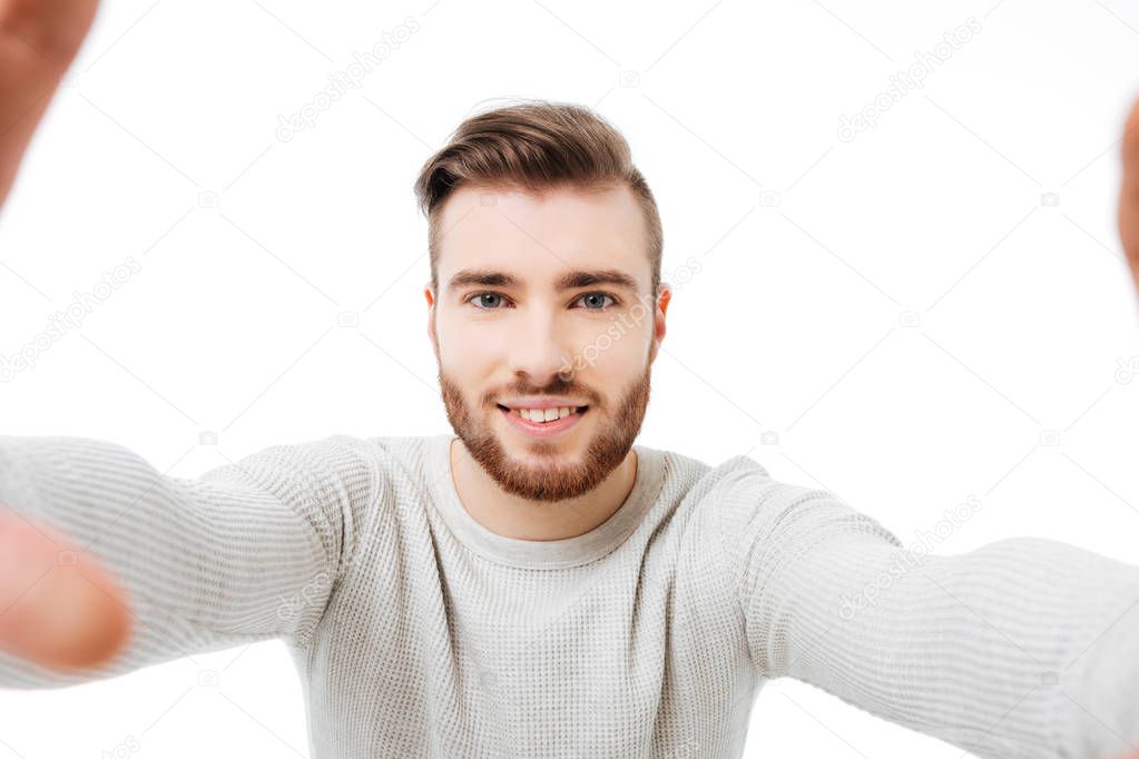 Young attractive man taking selfie over white background. Front camera view