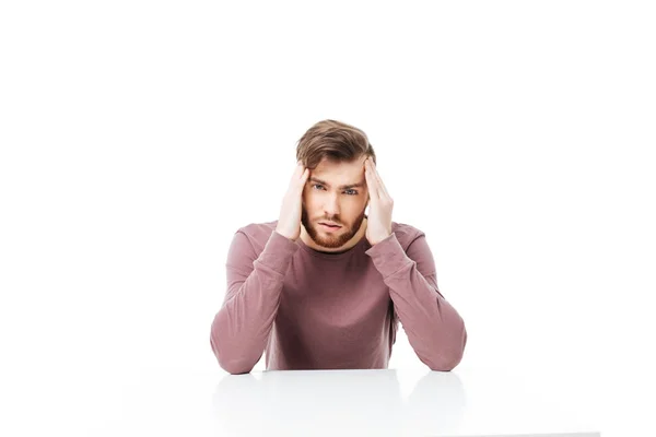 Young man showing headache or thinking gesture sitting at the table isolated — Stock Photo, Image