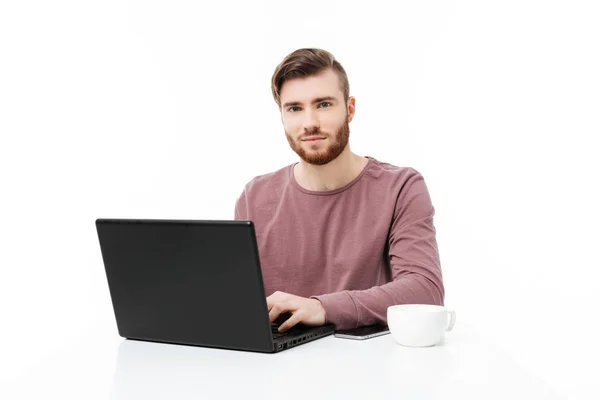 Bonito jovem na mesa olhando para a câmera trabalhando no computador portátil isolado — Fotografia de Stock