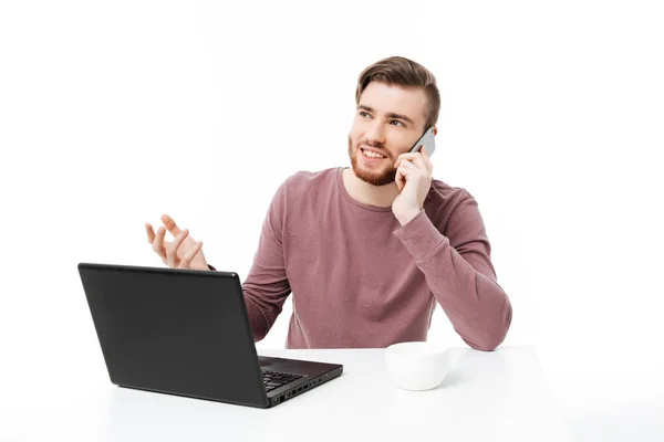 Schöner junger Kerl, der am Laptop arbeitet, am Telefon telefoniert und mit offener Handbewegung isoliert aufblickt — Stockfoto