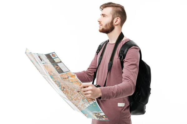 Joven hombre soñando mirando a un lado con el mapa abierto en las manos y la mochila sobre fondo blanco. Retrato de niño de pie con cámara y mochila negra aislada — Foto de Stock