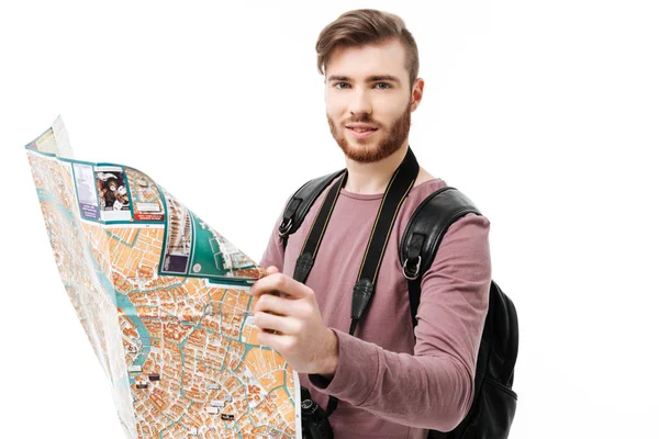 Joven hombre sonriente de pie con la cámara y el mapa en las manos sobre fondo blanco. Niño feliz mirando en cámara con mochila negra, cámara y mapa de carreteras aislados — Foto de Stock