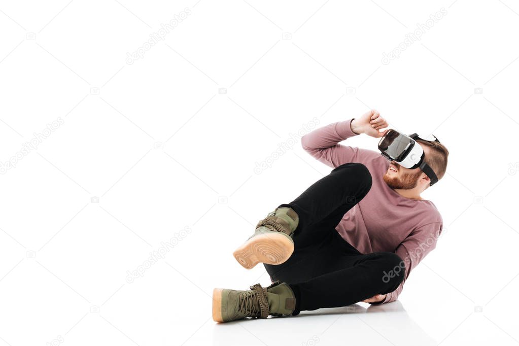 Young man sitting in studio and take cover of something while playing with virtual reality glasses on white background. Afraid boy using visual reality glasses isolated
