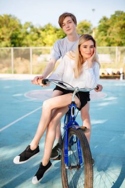 Güzel erkek ve kız sersem kamera basketbol sahasına vakit süre seyir bisiklet üzerinde sarı saçlı. Mavi Bisiklet park ile genç güzel çift portresi