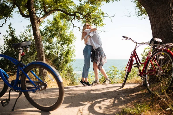 배경에 놀라운 바다 전망 공원에 서 있는 동안 서로 포용 하는 아름 다운 부부의 초상화. 옆에 빨간색과 파란색 클래식 자전거와 함께 시간을 보내는 젊은 귀여운 커플 — 스톡 사진